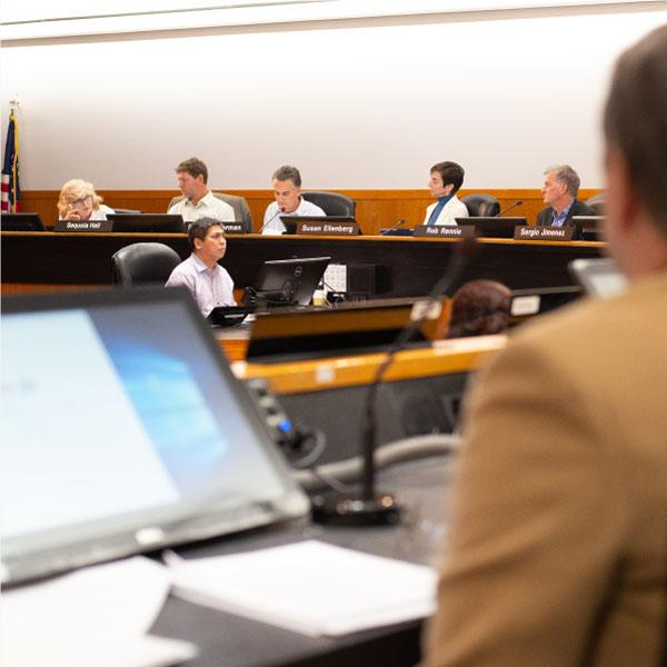 A commission meeting with commissioners seated at desks.